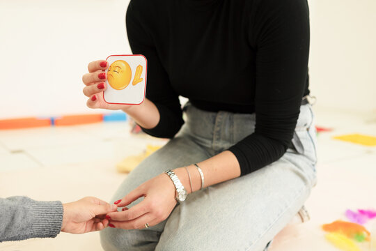 A therapist conducts a social skills training session using emoji cards to help a child identify facial expressions and emotions, focusing on behavioral development.