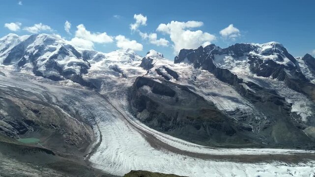 Aerial view of the Gornergrat glacier with snow-capped peaks, rocky mountain slopes, and deep glacial ice formations under a clear blue sky in Zermatt, Valais, Switzerland.