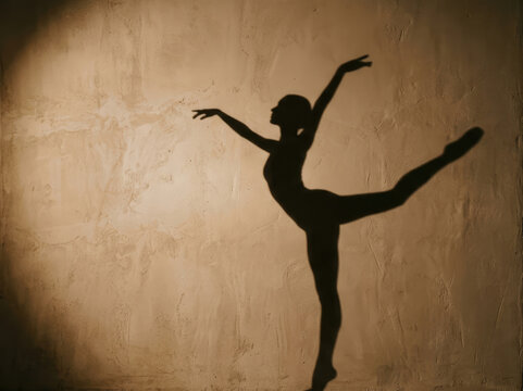A ballerina silhouette gracefully performs a d&eacute;velopp&eacute; pose against a textured, beige wall. The dancer&rsquo;s extended leg and raised arm create a dynamic and elegant form.