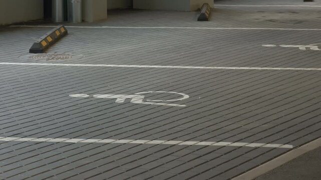 Empty indoor parking garage with gray tiled pavement, painted space markings, wheel stops, clean geometric lines, quiet urban setting, and practical vehicle access