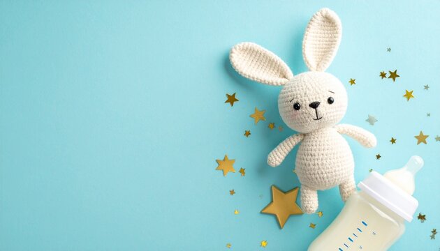 Top view photo of knitted bunny toy milk bottle and gold stars on isolated pastel blue background with copyspace