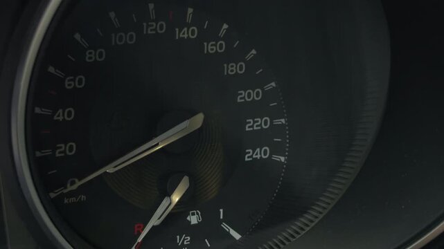 Car speedometer dashboard with glowing warning indicator, fuel gauge, and needle near zero, showing vehicle status panel inside dark interior with clear gauge markings and illuminated caution symbol