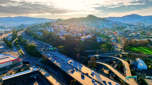 Multilane freeway interchange through San Francisco residential district at dusk. Highway overpass with moving vehicle, tree lined neighborhood and hill silhouette under soft diffused light.