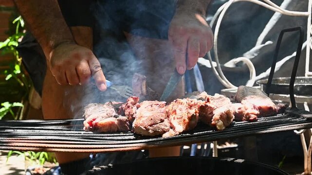 Parrillero acomodando carne vacuna sobre parrilla durante preparaci&oacute;n de asado argentino tradicional