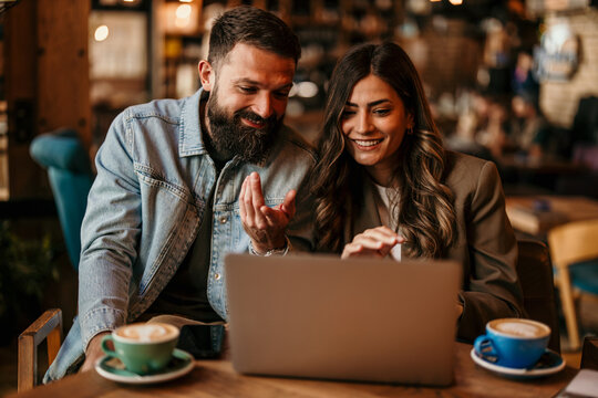 Smiling couple collaborating on laptop in coffee shop