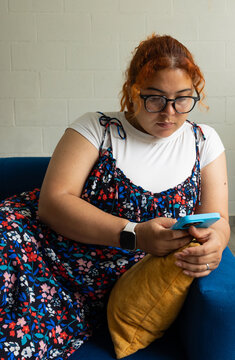 Woman sitting on the sofa at home looking at her mobile phone. Concept of digital communication, technology, connectivity, and everyday life at home