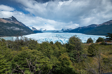 Naklejka premium Dramatic Glacier Landscape Under Cloudy Sky with Forest and Mountains