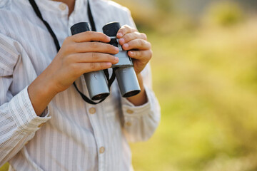Fototapeta premium Midsection of a little boy standing in a field with a binoculars at summer