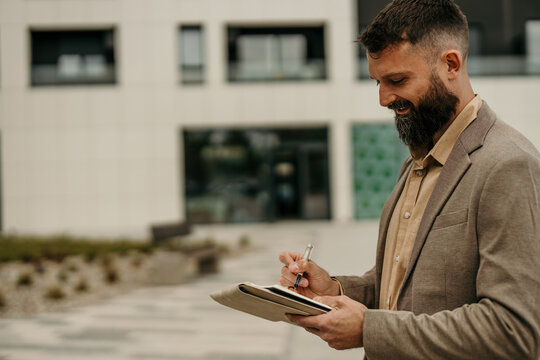 Professional man writing notes outdoors with notebook and pen