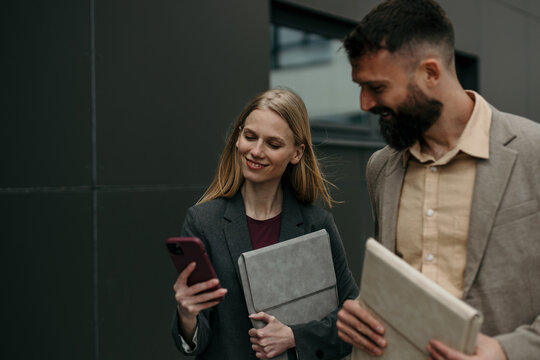 Business colleagues walking and reviewing content on phone