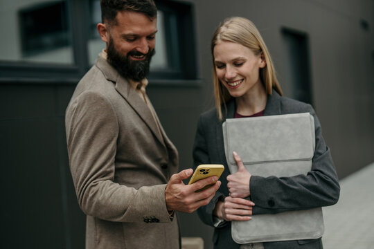 Business colleagues collaborating on smartphone outside office building