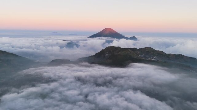 Aerial view of the volcanic peak of Mount Sindoro rising above a thick layer of clouds during sunrise in Indonesia.