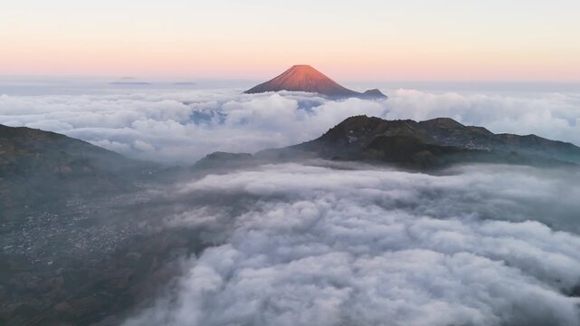 Aerial view of Mount Sindoro volcano peak rising above a dense sea of clouds during the golden hour in the highlands of Indonesia.