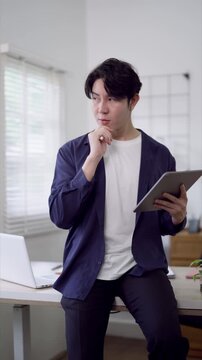 Young Asian freelance professional reviewing tablet application while working at modern bright home office desk