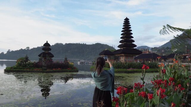 Female tourist taking a picture with a smartphone of a famous hindu water temple in indonesia