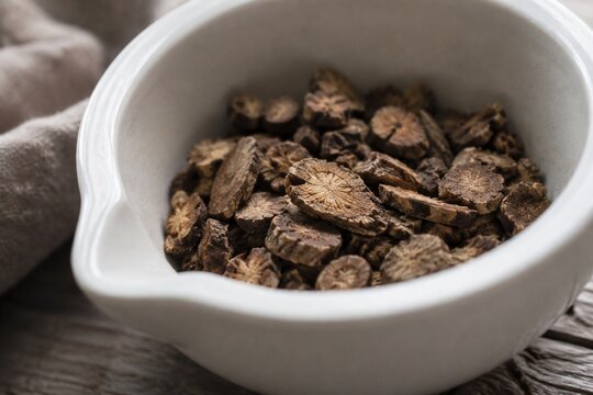 Dried slices of valerian root scattered in a white ceramic mortar with soft natural side lighting.