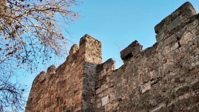 Low angle view of weathered medieval stone fortification wall with battlements against clear blue sky in antalya kaleici.