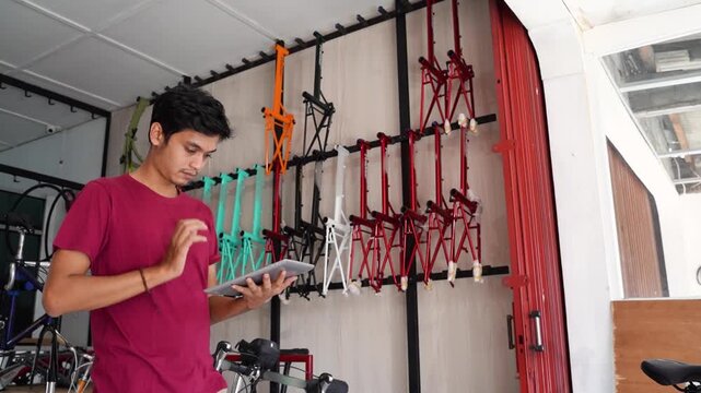 Near-end sequence shows man at left side, focused on smartphone inside bicycle workshop, with hanging bicycle frames, repair tools, and bright indoor light