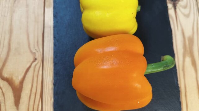 Multicolored bell peppers on flat black slate plate, top view