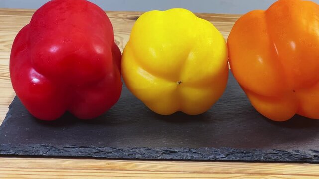 Multicolored bell peppers on flat black slate plate, side view