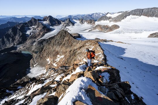 Mountaineer on a rocky ridge on the Wilder Freiger summit, behind him Signal summit and Becher summit with Becherhaus, picturesque high mountain landscape, view of &Uuml;beltalferner glacier and rocky mountain peaks K&ouml;nigshofspitz and Sonklarspitze, Stubai Alps, South Tyrol, Italy