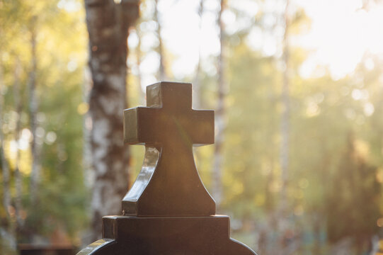 Traditional Orthodox cemetery with an ancient stone cross illuminated by warm sunbeams through green trees