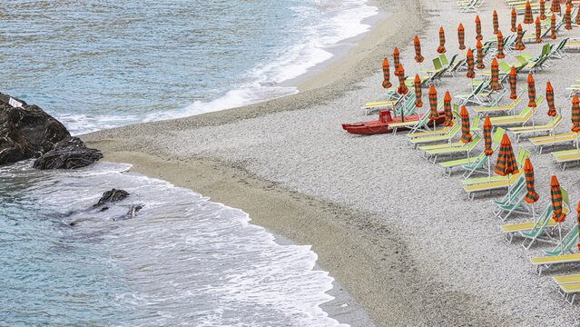 Sun loungers and parasols, boulders on the beach di Fegina, behind the Torre Aurora Mare, Monterosso al Mare, Cinque Terre, Ligurian Coast, Liguria, Italy