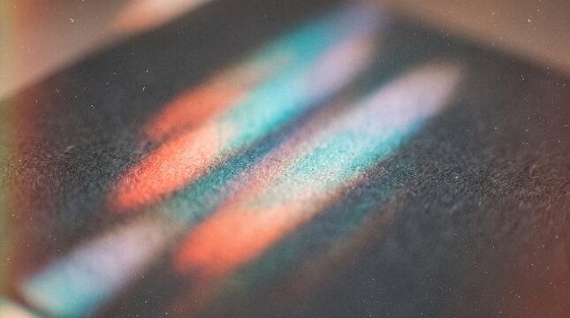 Parallel prismatic light refraction bands casting bright turquoise and coral red stripes across a rough dark texture