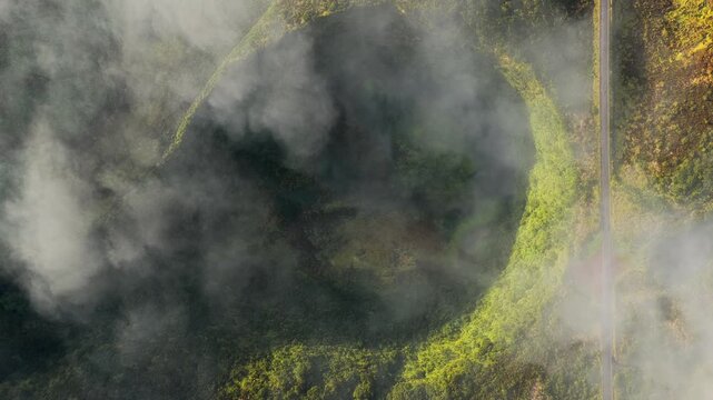 Aerial view of the volcanic crater on Flores Island surrounded by lush green vegetation and clouds in Azores, Portugal.