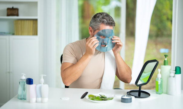 Man applying facial cream during a morning beauty routine at home. Male beauty model using a moisturizing mask for skincare and rejuvenation. Male cosmetic facial treatment for aged skin.