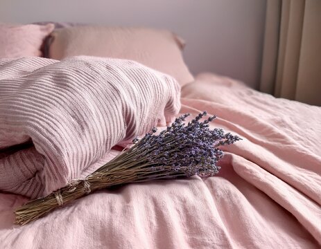 close up of soft dusty rose pink linen bedsheets with a sprig of lavender on the pillow and a folded cream knitted throw blanket elegant bedroom and home decor concept horizontal