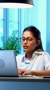 Indian businesswoman drafting email on laptop at desk in modern cozy office, Asian young female corporate executive typing an important message while thinking working remotely on wireless computer