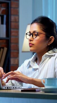 Indian businesswoman drafting email on laptop at desk in modern cozy office, Asian young female corporate executive typing an important message while thinking working remotely on wireless computer