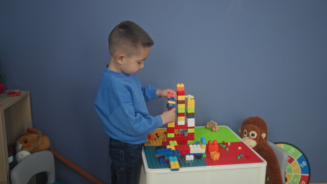 Hispanic boy carefully stacking colorful plastic blocks with hands into a tall tower on a play table in building; quiet concentration.