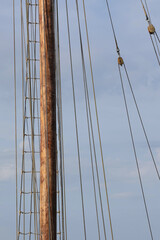 Obraz premium Tall sailing ship mast and rigging with rope ladder and sail ropes against a blue sky in a harbour