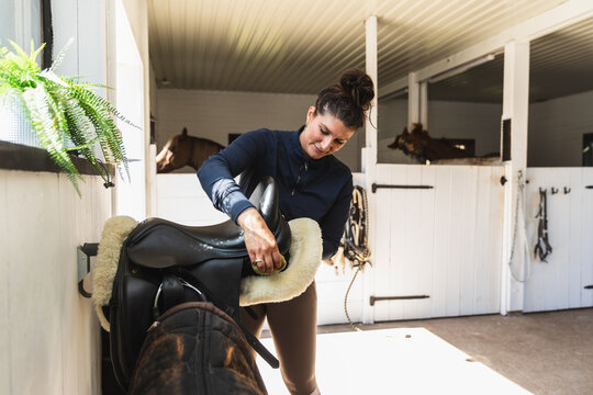 Woman Polishing Leather Saddle in Tack Room