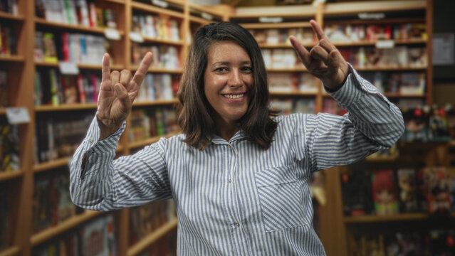 Woman shows rock horns with both hands in a bookstore aisle inside a building; playful celebration moment.