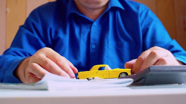 Stressed car insurance agent nervously playing with yellow toy car at desk close up. Focus on hands and vehicle, shallow DOF. Anxious businessman feeling pressure at work.