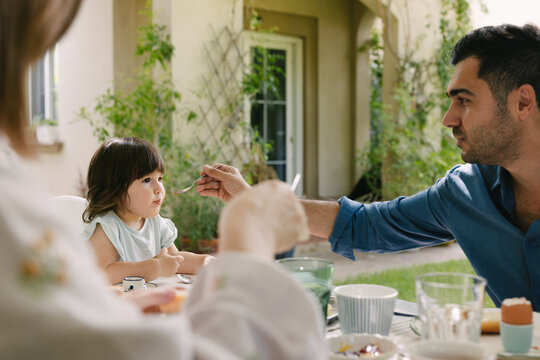 Father and mother with a toddler having breakfast in the garden