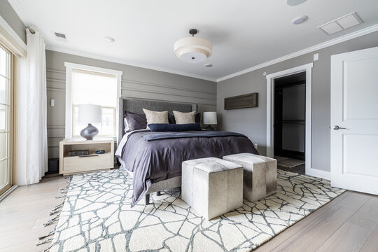 Modern Gray Bedroom with Dark Bedding, Upholstered Ottomans and Patterned Rug