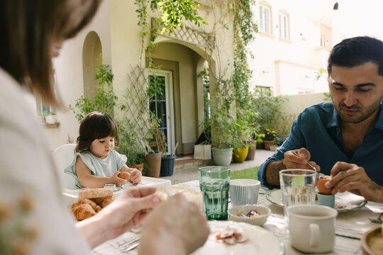 Father and mother with a toddler having breakfast in the garden