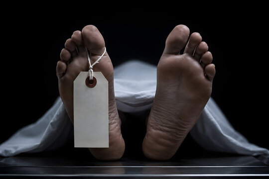A somber close-up of a deceased person's feet with a blank identification cardboard toe tag, emerging from a white sheet on a metal table against a dramatic black background