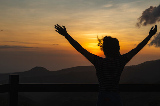 Individual embracing freedom watching sunset over mountains