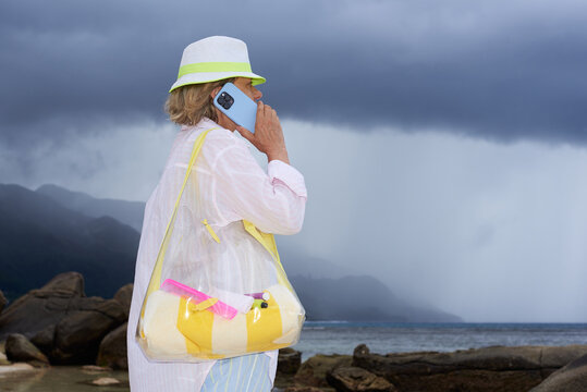 Woman talking on phone at beach under dark clouds