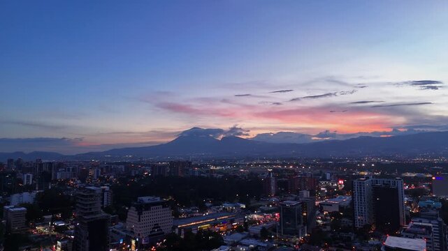 Vista panor&aacute;mica de Ciudad de Guatemala al atardecer con edificios corporativos y volcanes de fondo.