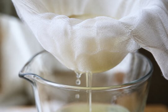 Fine cheesecloth straining liquid into a clear glass vessel, detail shot.