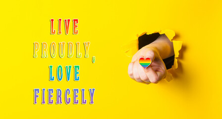 Fototapeta premium Hand Holding Rainbow Heart Through Yellow Paper with Inspirational Text