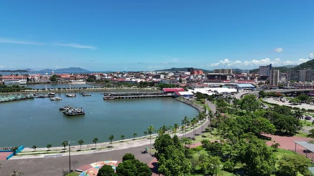 Cinematic drone footage flying from the Cinta Costera waterfront beside Panama City's famous Fish Market (Mercado de Mariscos) toward the historic Casco Viejo. Beautiful aerial panorama 
