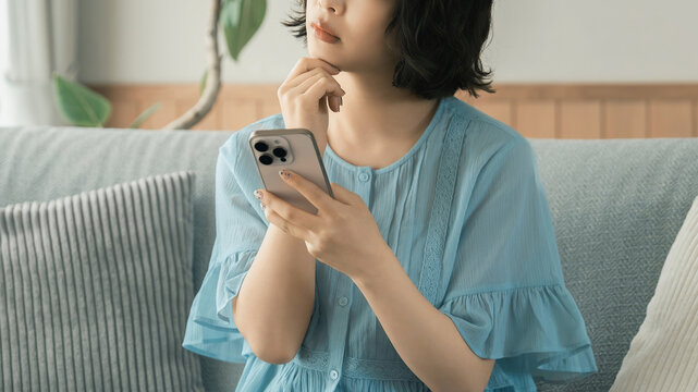スマートフォンを見ながら考える女性, Thoughtful Woman Looking at a Smartphone