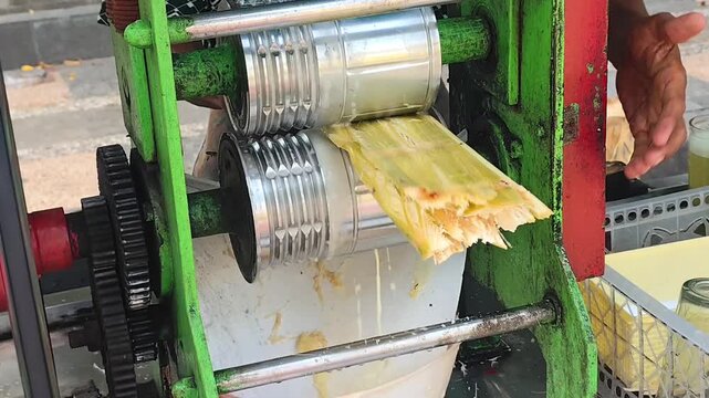 Close-up of a manual sugarcane juice machine extracting fresh juice from sugarcane stalks, demonstrating the production process of a popular street food beverage